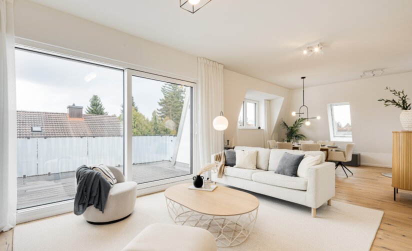 Foto eines Wohnzimmers mit Sofa und Esstisch im Dachgeschoss einer bezugsfertigen Neubauwohnung in Trudering von Domino Bau, mit Blick auf die Loggia